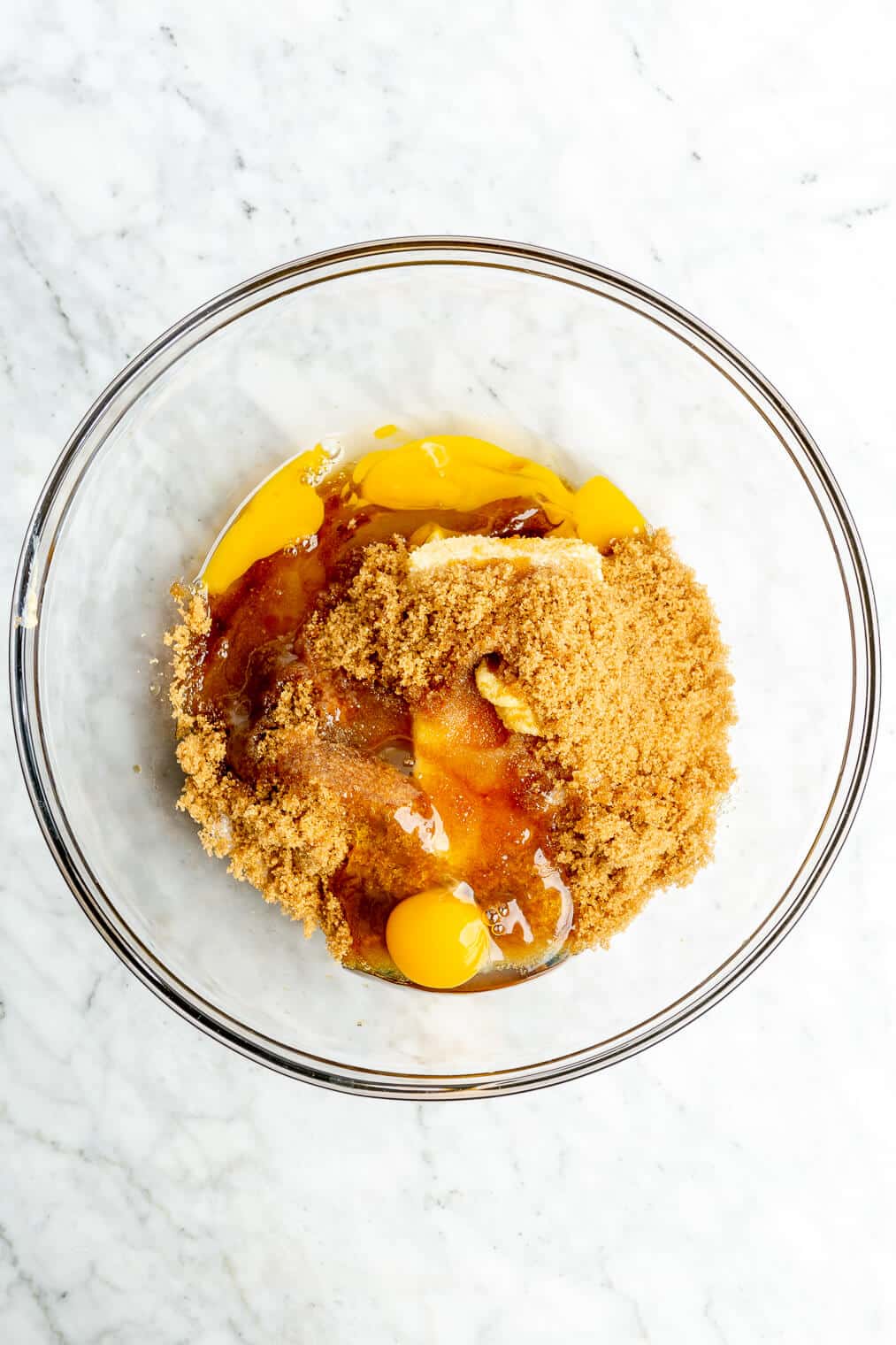 A large glass bowl of softened butter, white sugar, brown sugar, eggs, and vanilla extract.