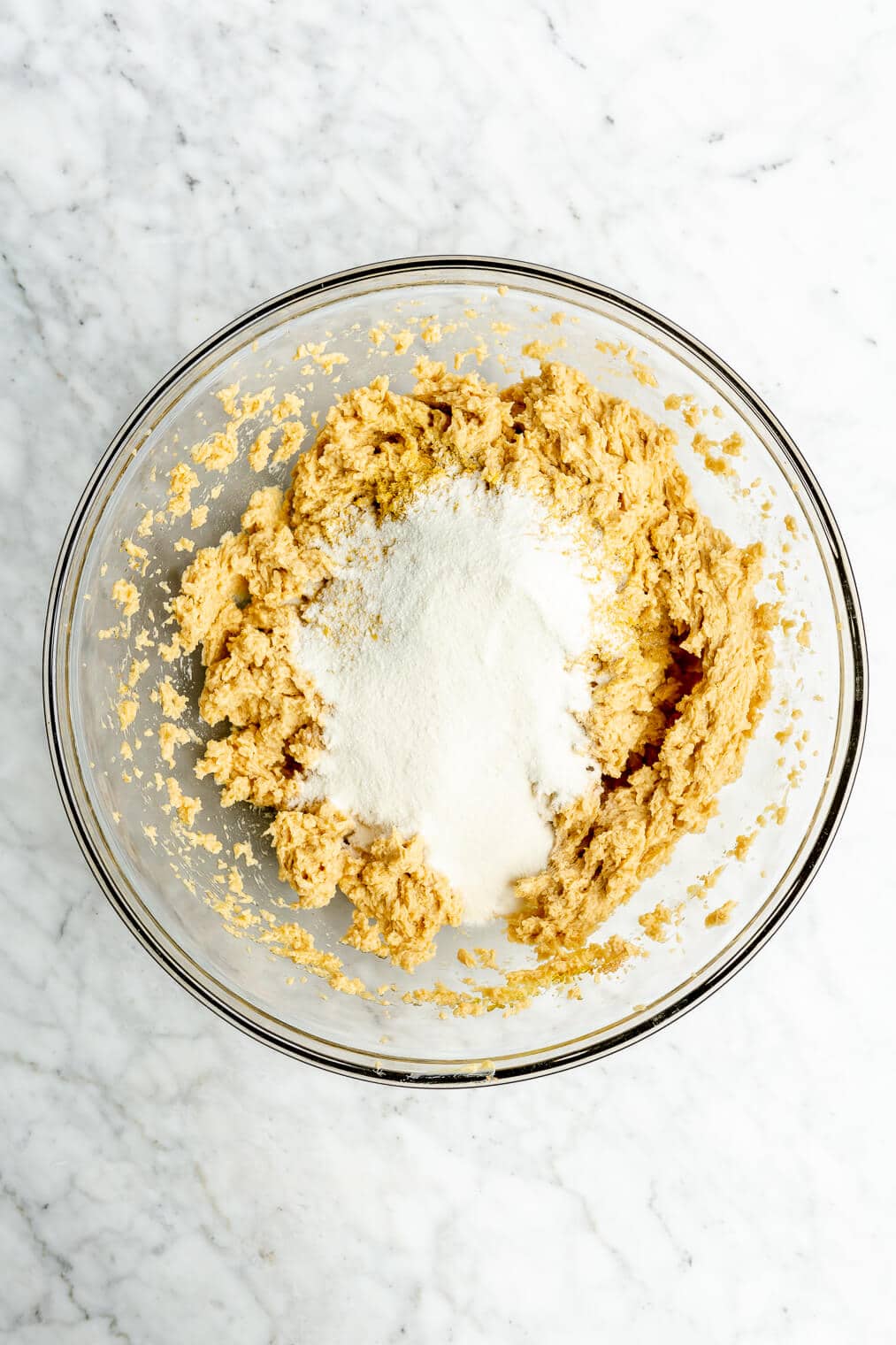 A top view of cassava flour sitting in a bowl of the whipped wet ingredients for cookie dough.