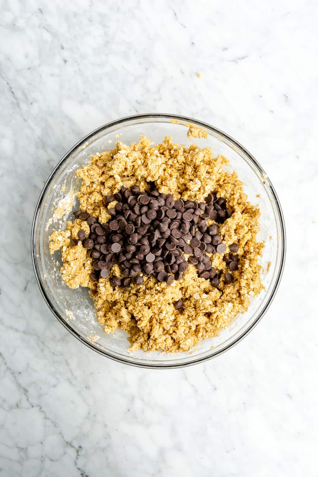 Top view of oatmeal cookie dough topped with a bunch of chocolate chips in a large glass bowl.