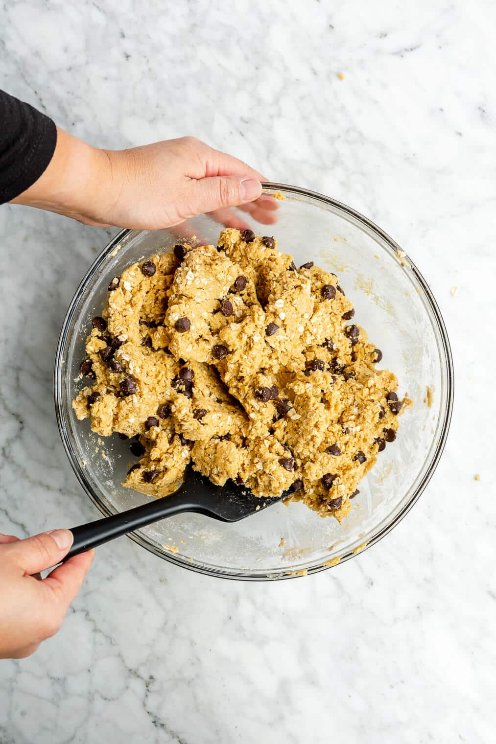 A person using a black spatula to stir chocolate chips into oatmeal lactation cookie dough.