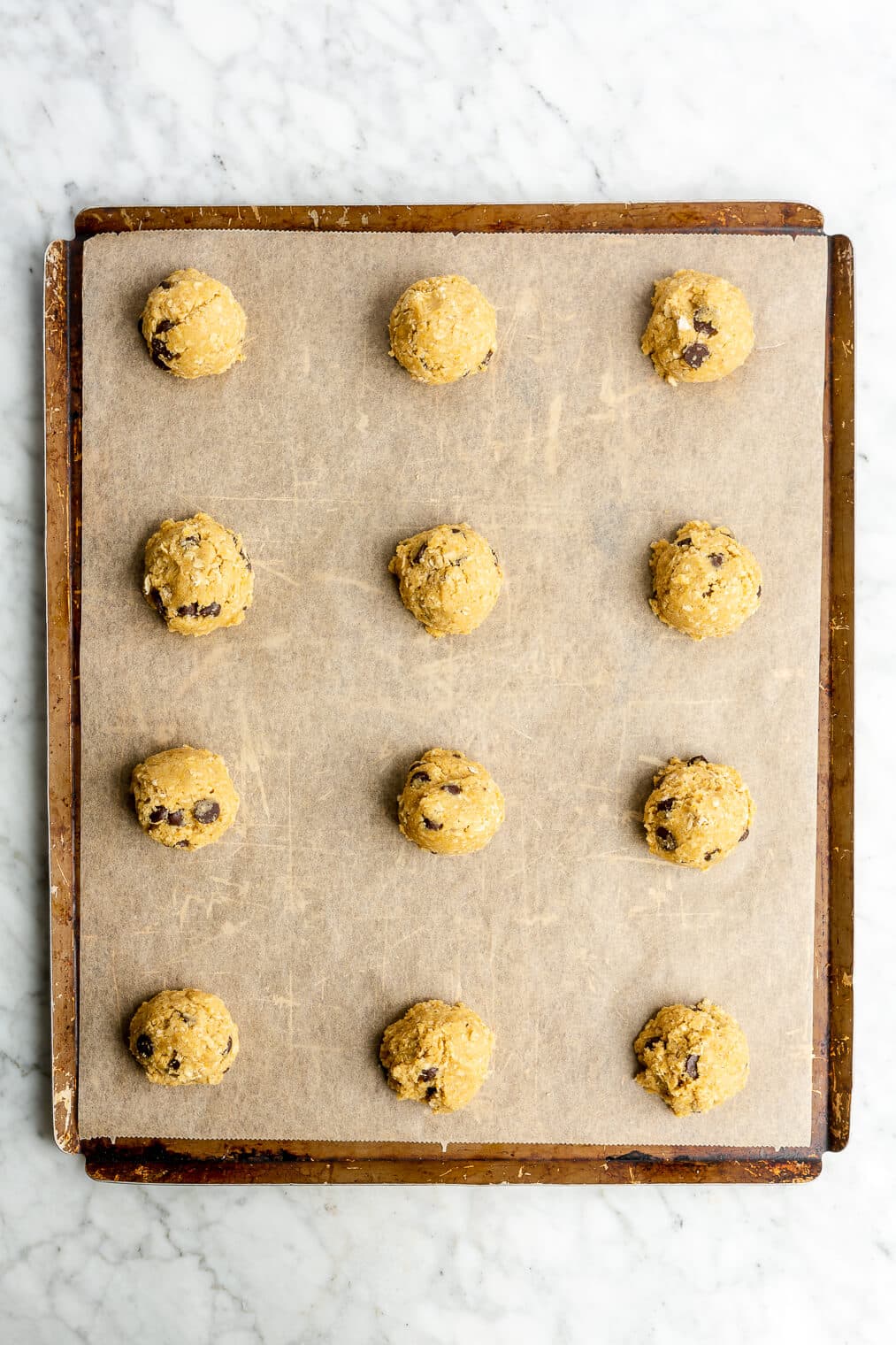 Scoops of cookie dough on a parchment paper lined cookie sheet.