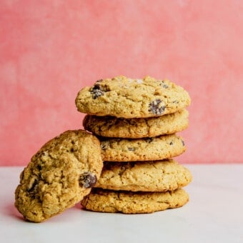 A stack of 6 oatmeal chocolate chip lactation cookies on a marble surface with a pink background.