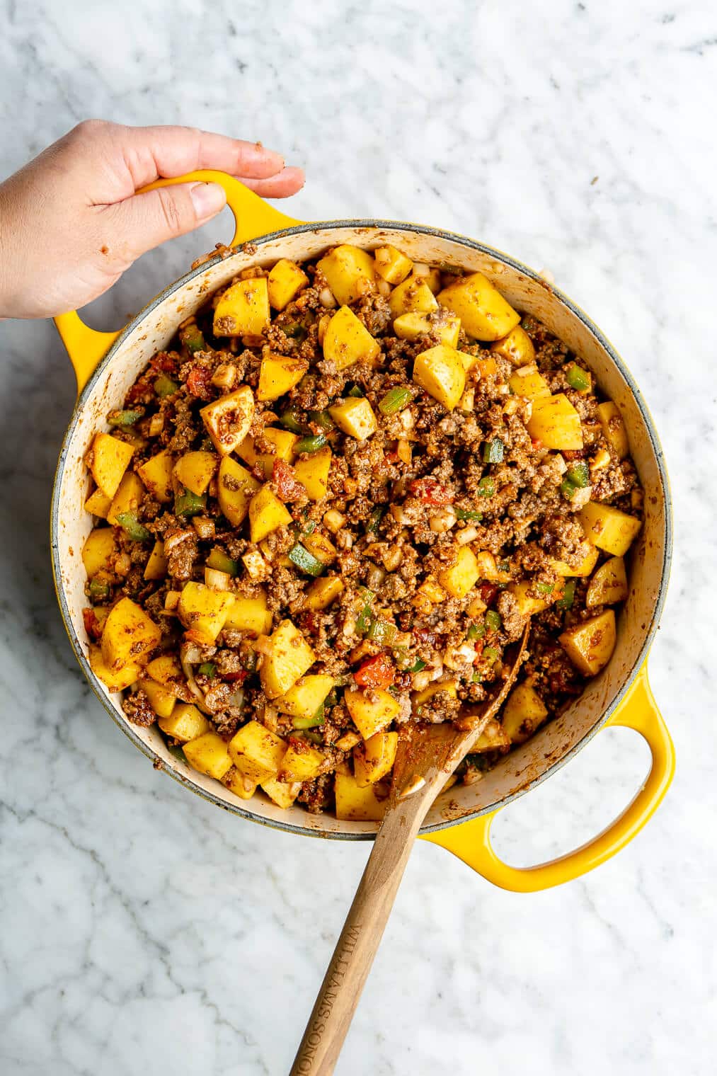 A large, yellow, enameled cast iron pot filled with Mexican picadillo. Also pictured: a wooden spoon sticking out of the pot