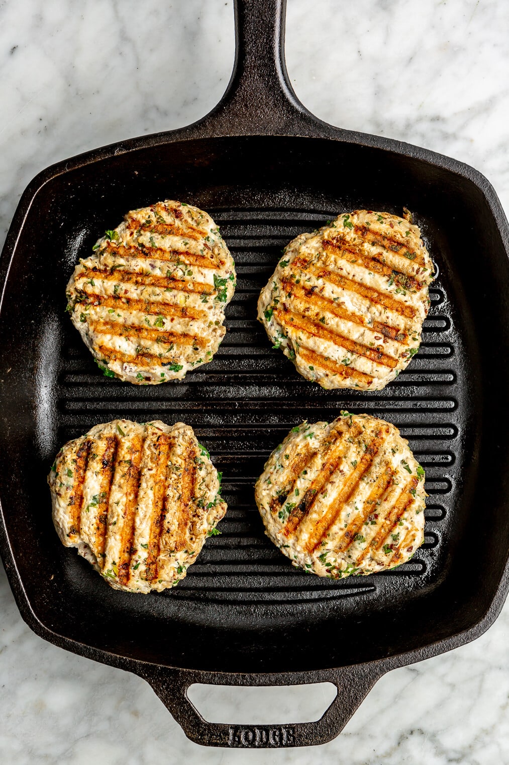 4 chicken burger patties being grilled on a cast iron grill pan.