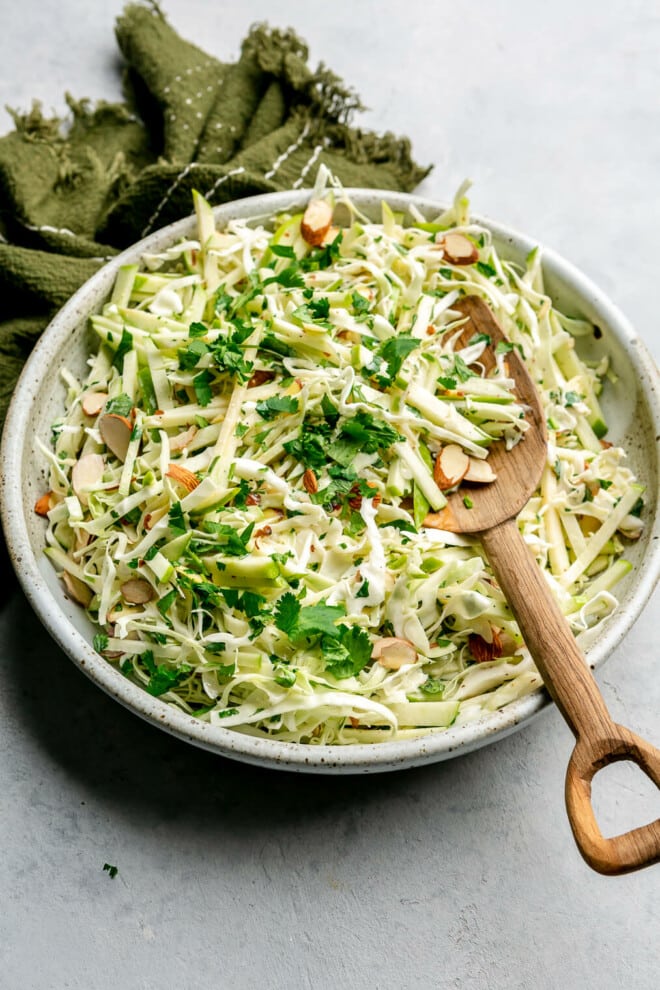 A top view of green apple slaw in a large decorative bowl with a wooden serving spoon.