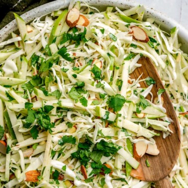 A top view of green apple slaw in a large decorative bowl with a wooden serving spoon.