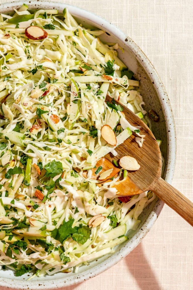 A top view of green apple slaw in a large decorative bowl with a wooden serving spoon.