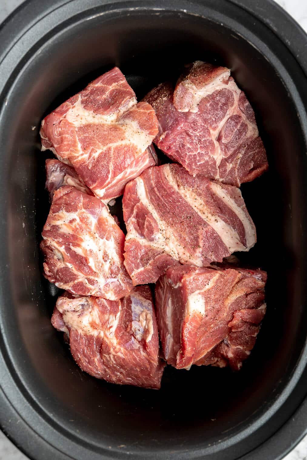 A large crock pot filled with chunks of raw pork butt.
