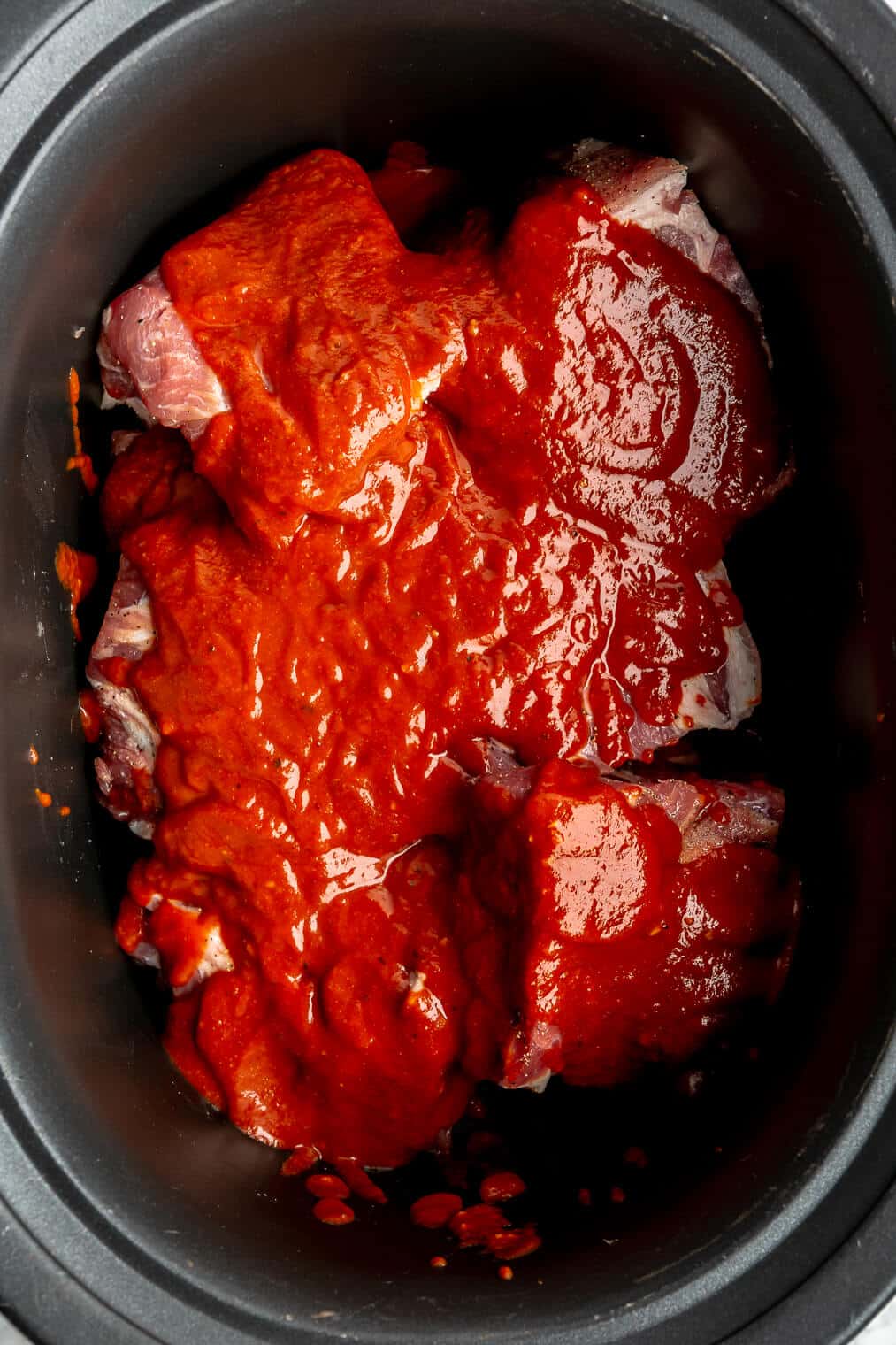 A large crock pot of raw pork butt covered in BBQ sauce.