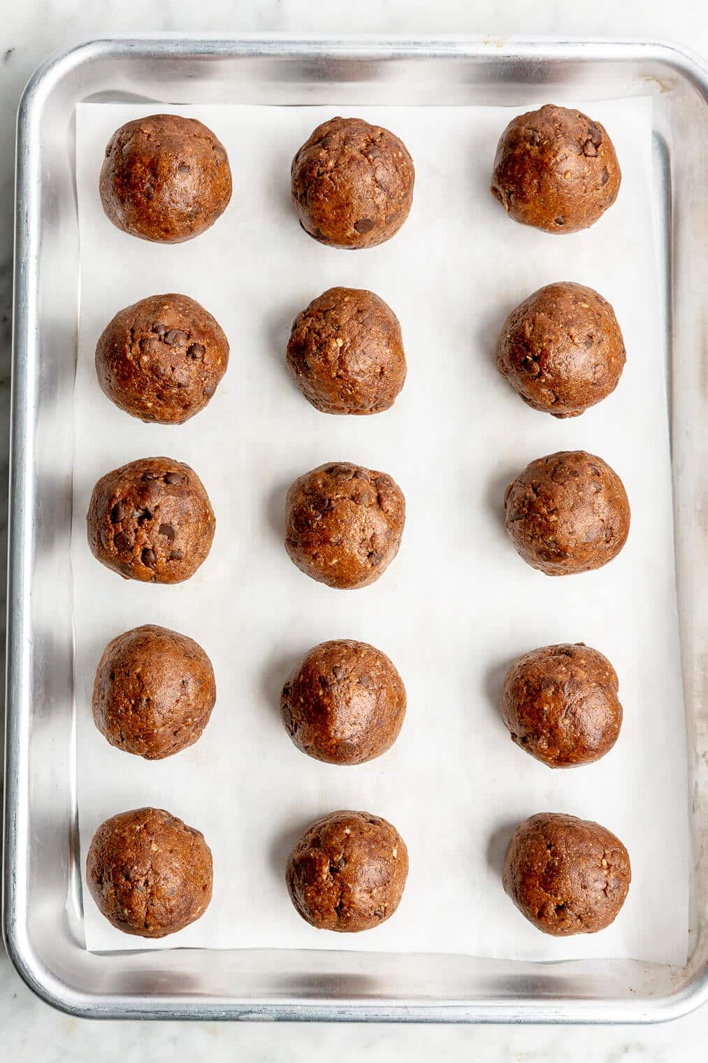 Chocolate date balls on a parchment paper lined sheet pan.