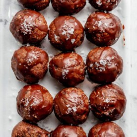 A sheet pan of chocolate date balls drizzled with chocoalte and topped with flaky sea salt.