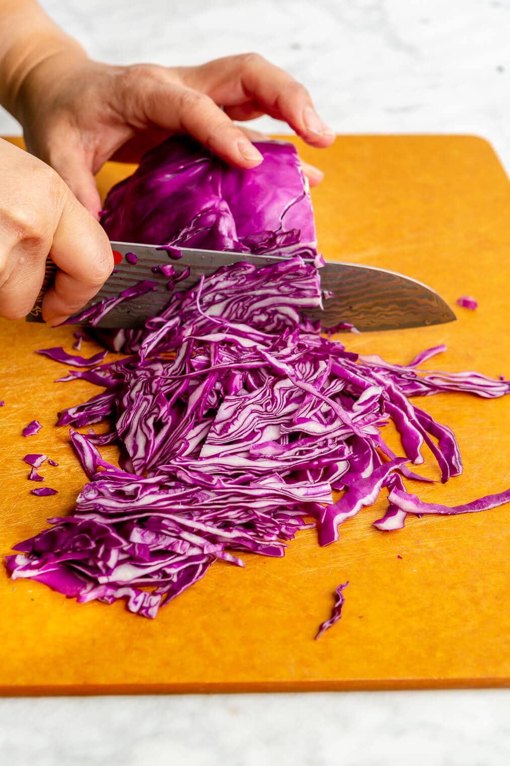A person chopping purple cabbage on a cutting board for easy slaw.
