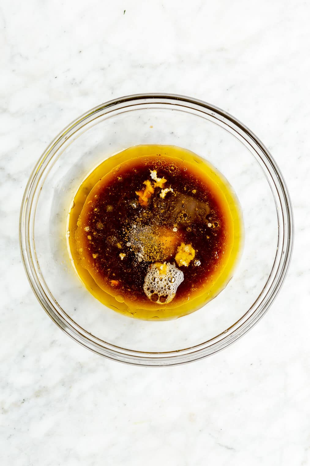 A top view of a small glass bowl of salt, pepper, grated garlic, olive oil, and coconut aminos.