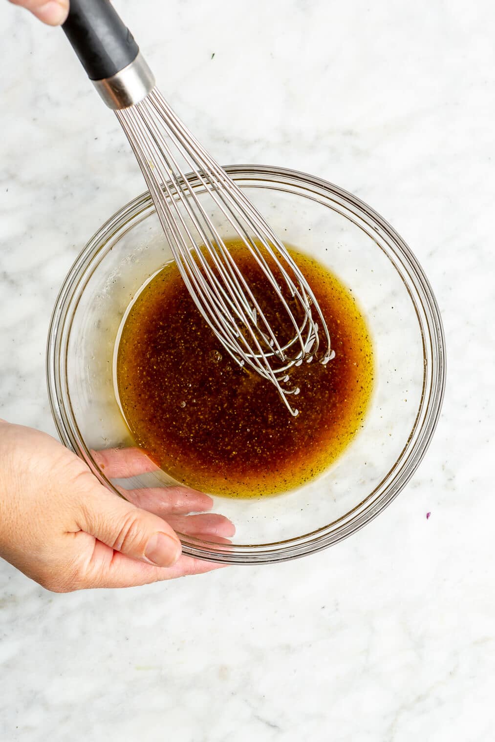 A person using a whisk to stir together a brown colored dressing for an easy, healthy, slaw.