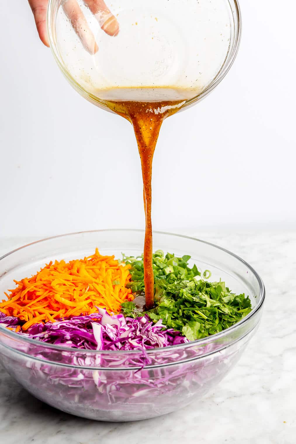A person pouring a brown colored dressing over a bowl of easy, healthy slaw.