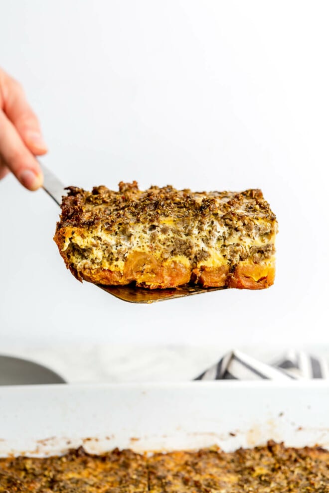 A person holding up a slice of plantain breakfast casserole with a spatula.