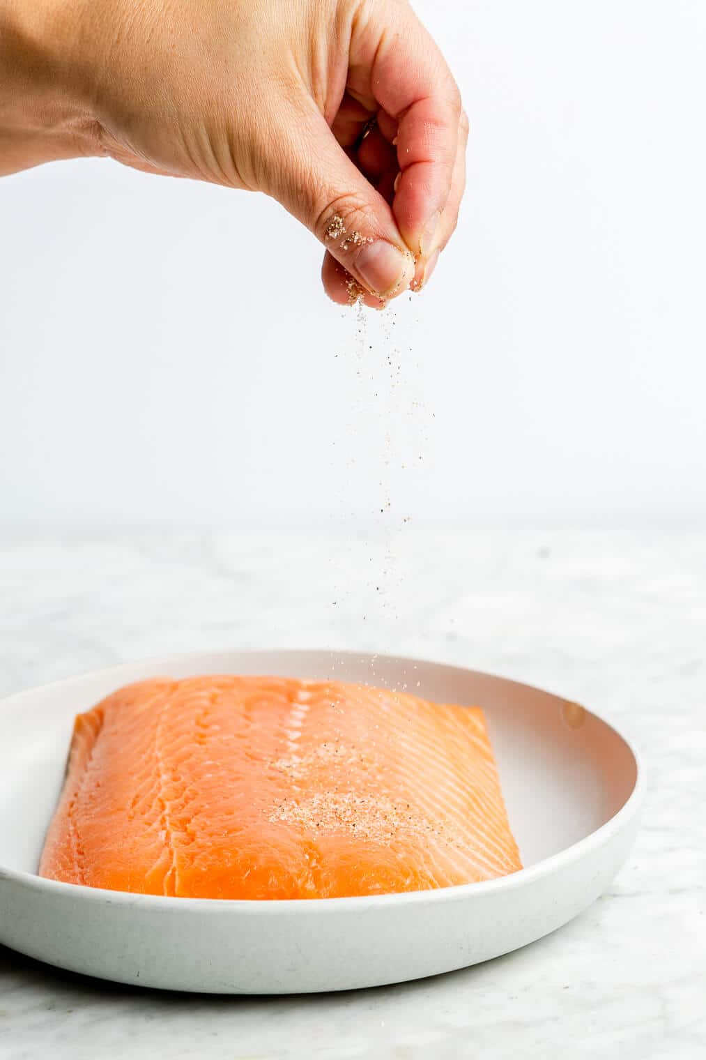 A person sprinkling seasoning onto a filet of salmon.