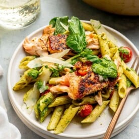 A plate of salmon pesto pasta next to a large pan of salmon pesto pasta.