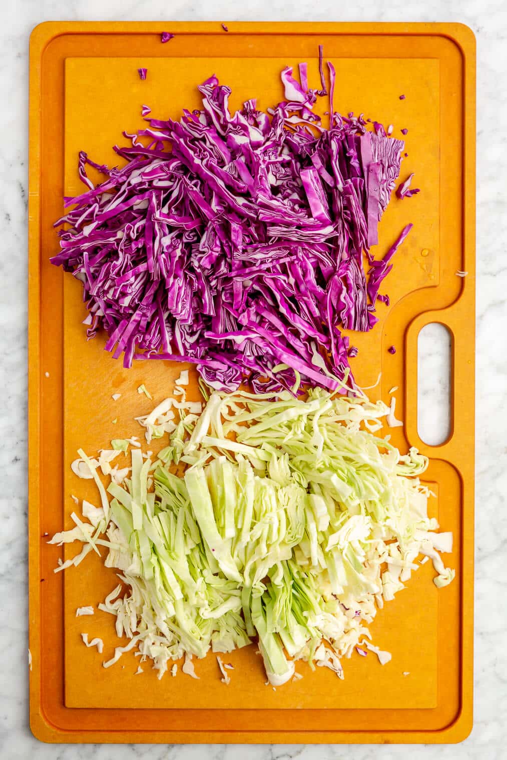Shredded purple and green cabbage on a large epicurean cutting board.