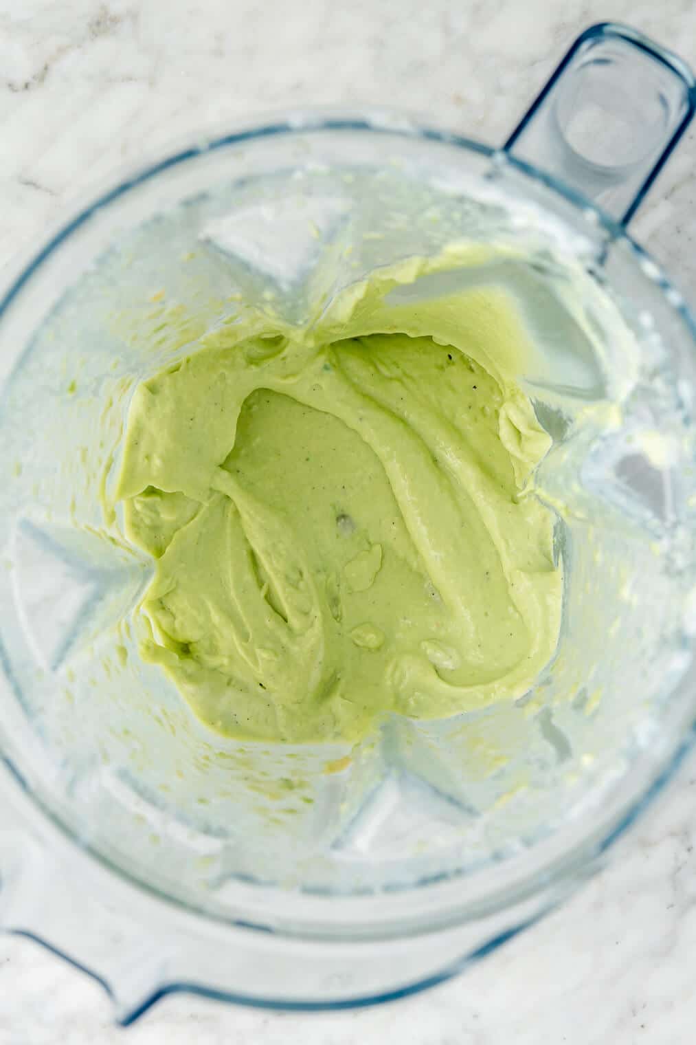 Avocado crema in a blender on a grey and white marble surface.