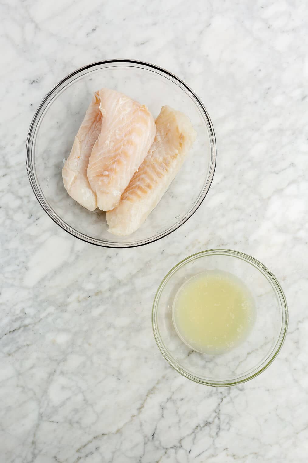 Cod in a large glass bowl next to a smaller glass bowl in lime juice.