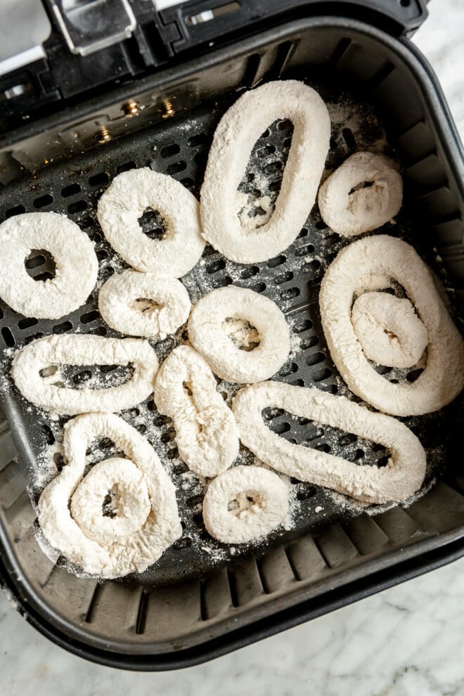 Raw, breaded calamari rings in an air fryer basket.