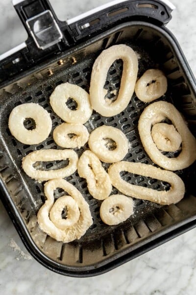 Calamari rings in an air fryer after cooking halfway through and being flipped over.