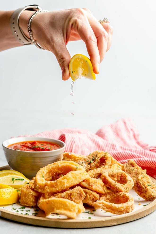 A person squeezing lemon juice over a plate of crispy fried calamari rings.