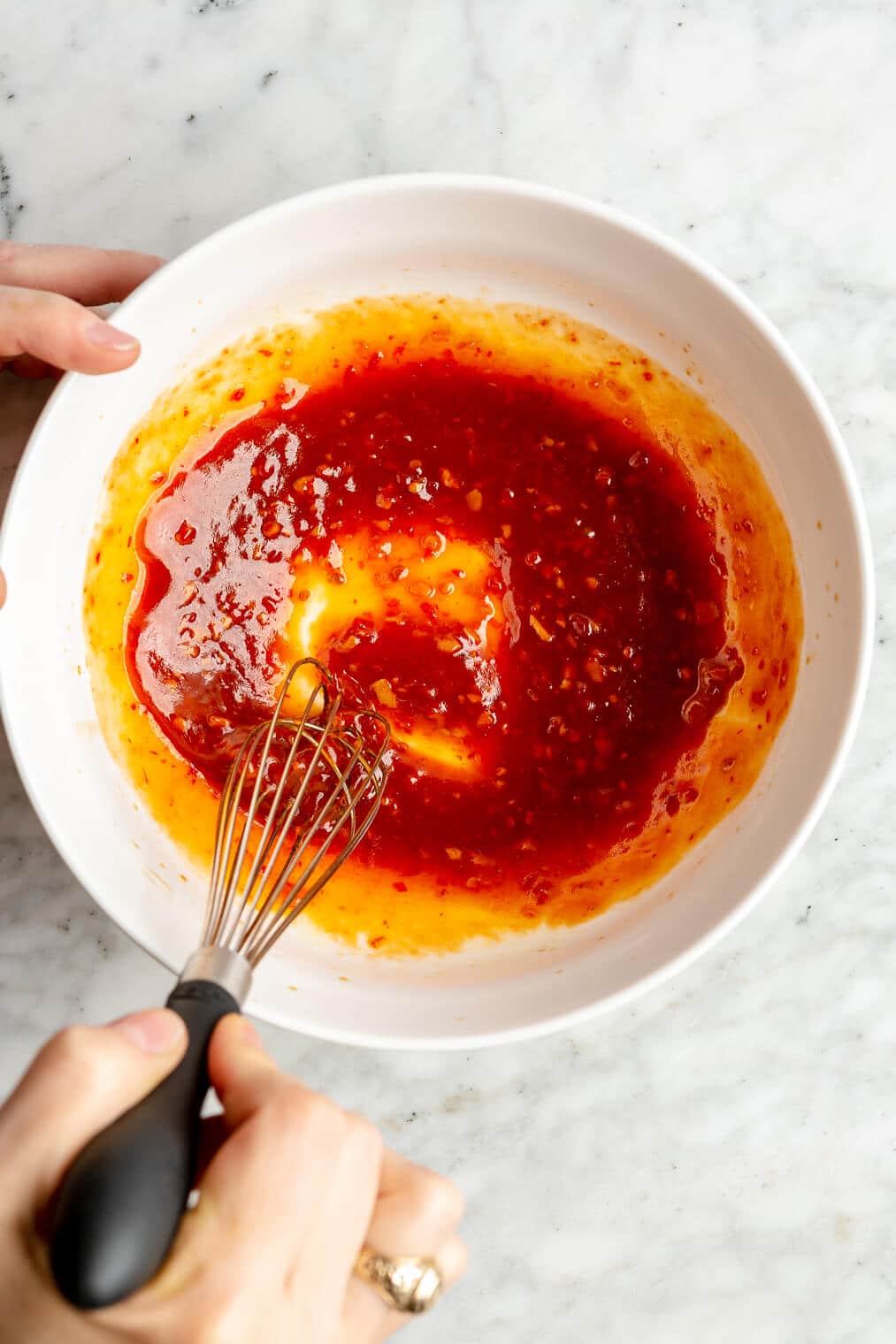 Hand whisking together chili-lime sauce in a white bowl.