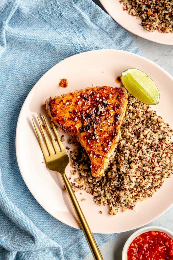 Chili-lime seared ahi tuna steak on a plate next to a bed of tricolor quinoa and a lime wedge.