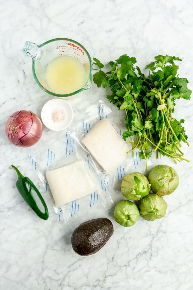 Fish ceviche ingredients on a grey and white marble surface.