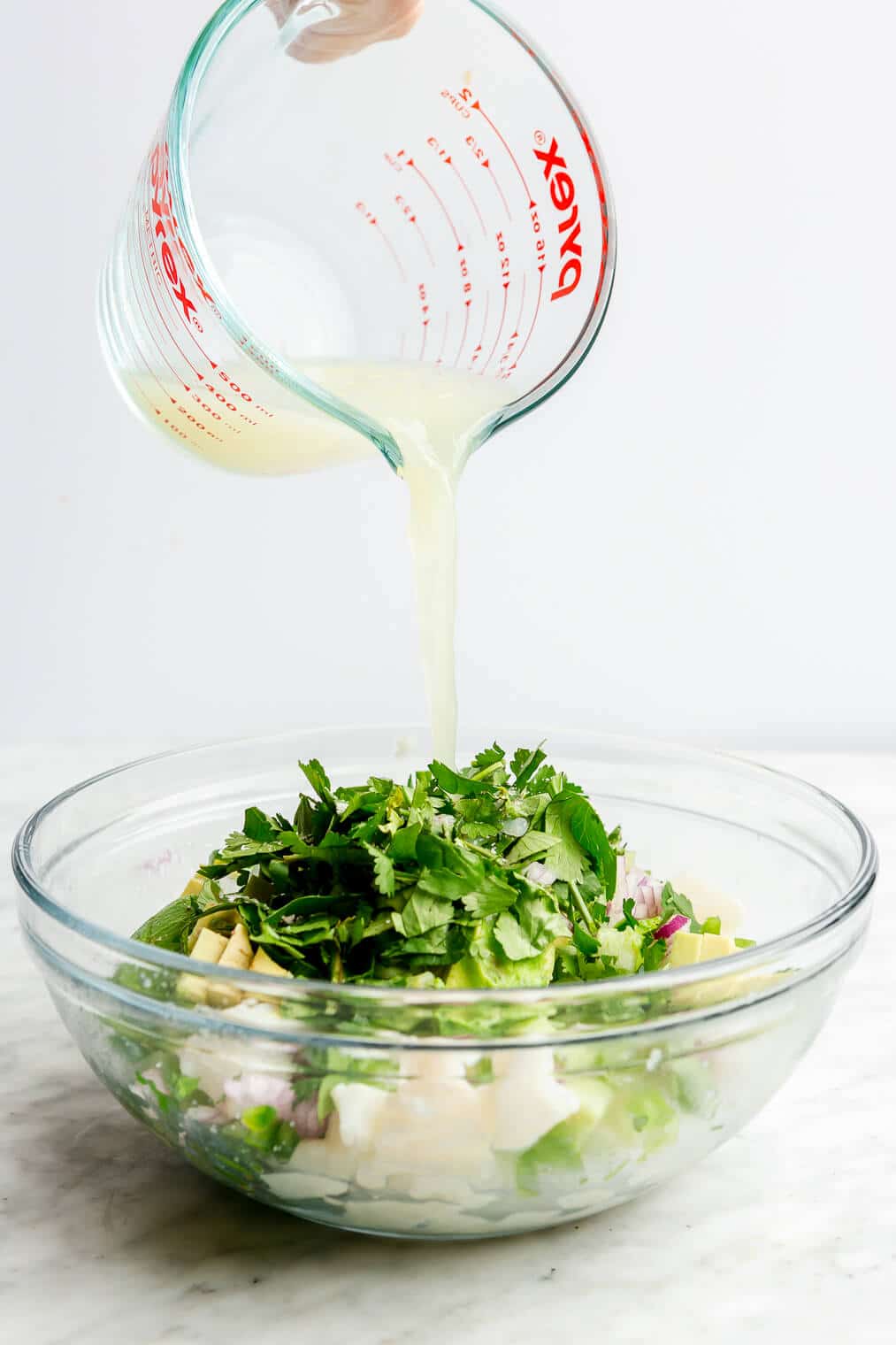 Hand pouring lime juice over a bowl of fresh cilantro, diced veggies, and cubed white fish.