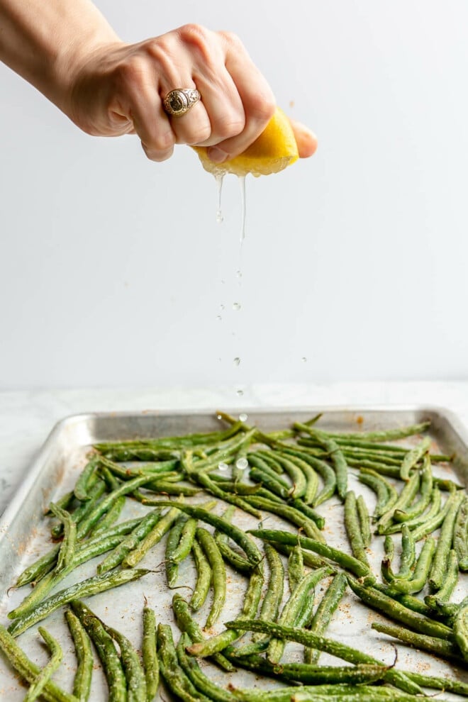 A person squeezing lemon juice over a sheet pan of oven roasted green beans.