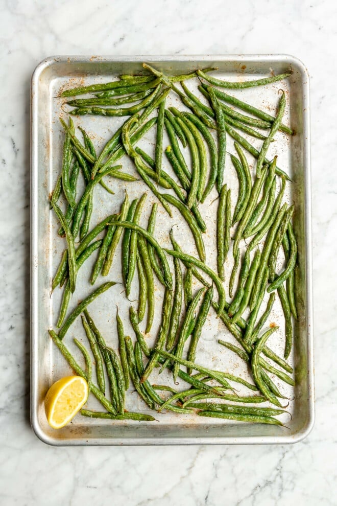 Top view of a sheet pan of roasted green beans with a squeezed halved lemon in the corner.