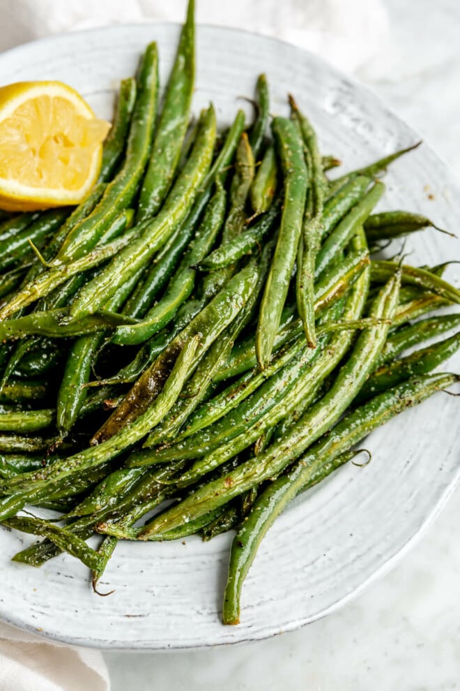 A white bowl filled with oven roasted green beans next to a squeezed halved lemon.