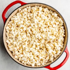 A red dutch oven with a white enamel interior with stove top popped corn in the pot.
