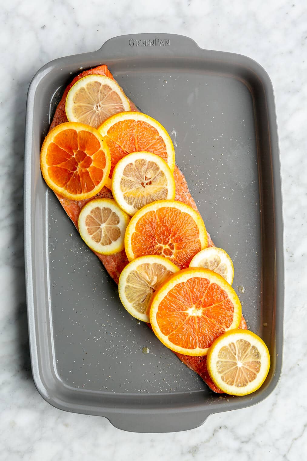 Salmon filet covered with citrus slices on a grey sheet pan.