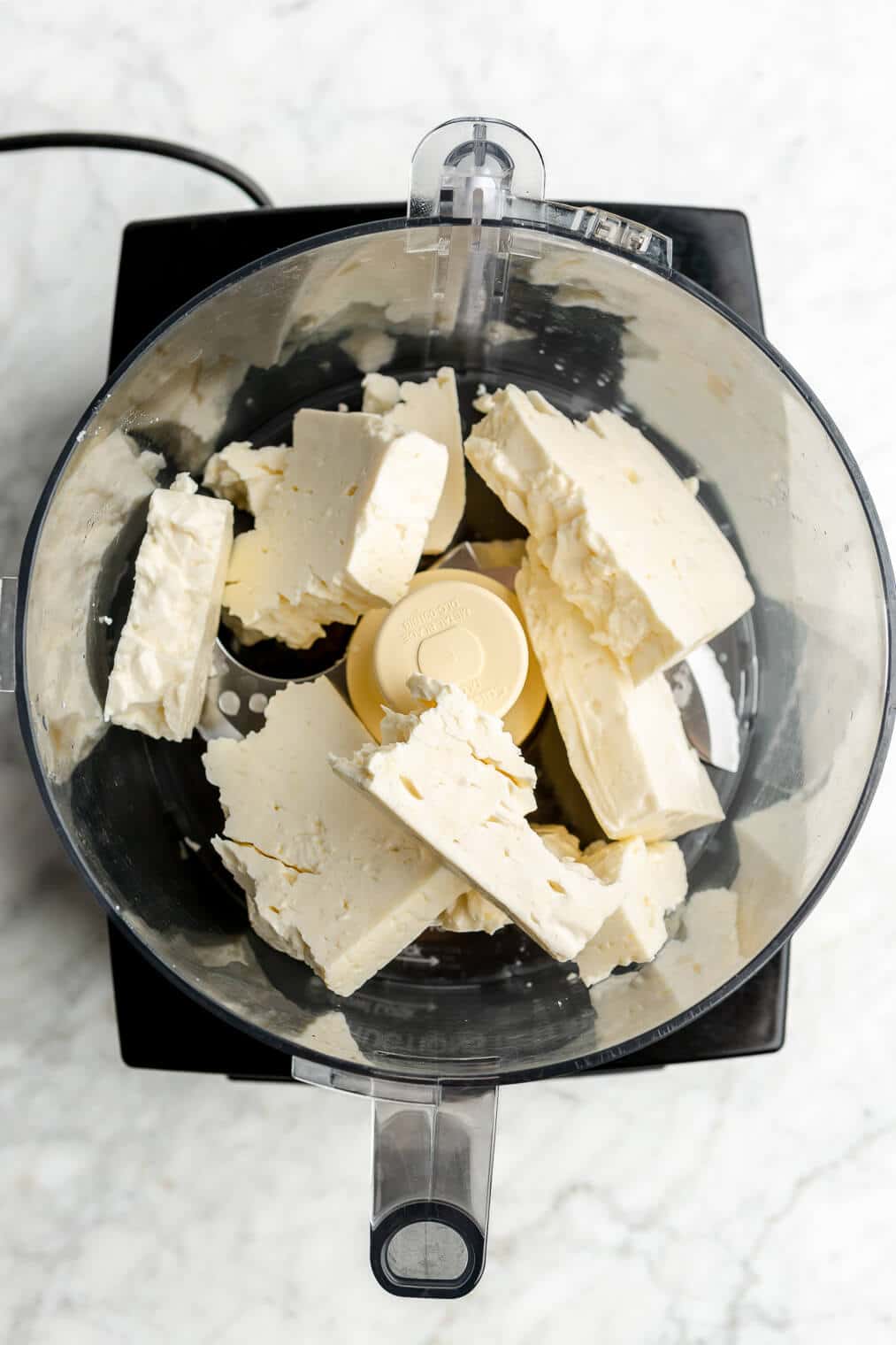 A couple blocks of feta cheese in a food processor.