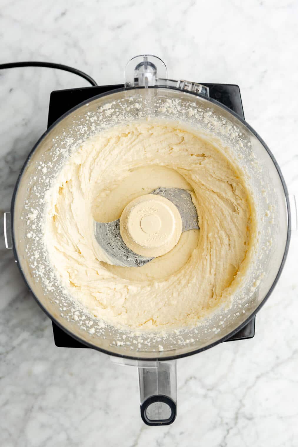 Top down of a food processor with blended feta and honey. The mixture is smooth.