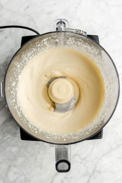 Top down of whipped honey feta mixture in a food processor on a grey and white marble surface. The mixture is smooth and creamy.