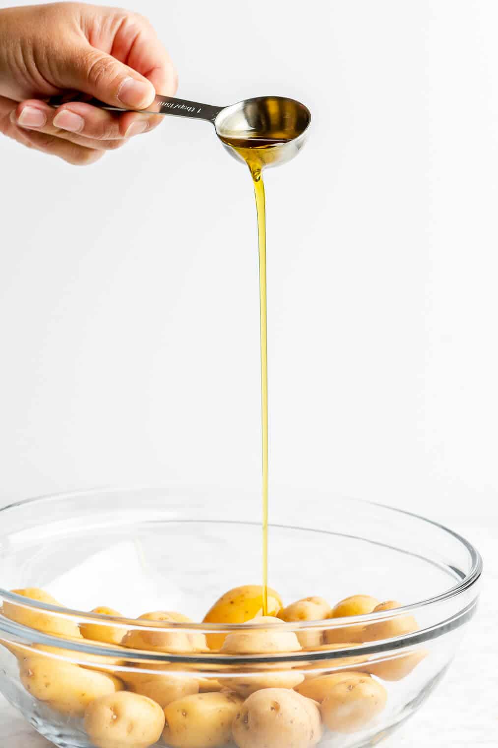 A person pouring olive oil into a bowl of baby potatoes.