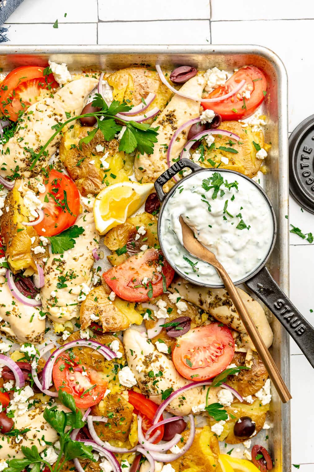 A Greek chicken sheet pan dinner with potatoes, chicken tenders, tomatoes, red onion, olives, and feta cheese.