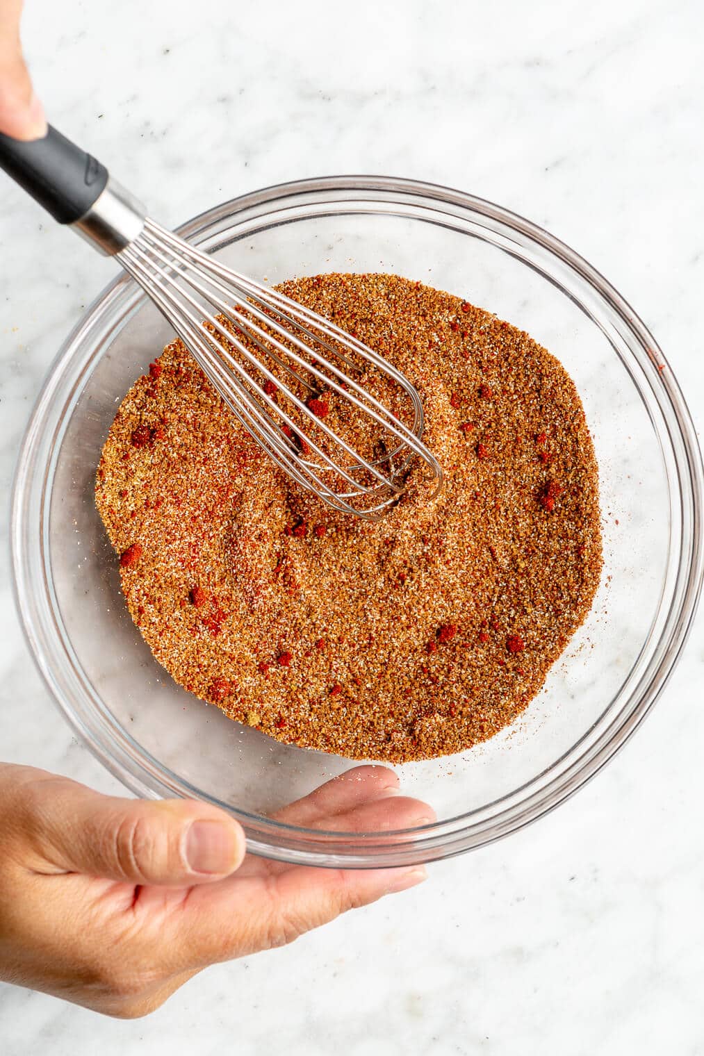 A person using a whisk to whisk together a pork spare rib BBQ spice rub.