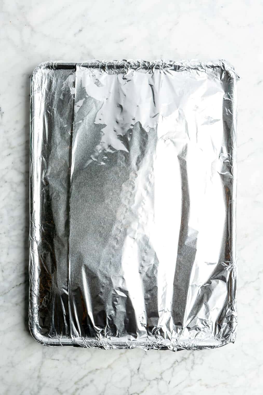Pork spare ribs wrapped in aluminum foil on a sheet pan.