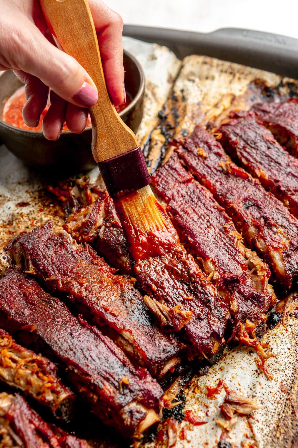 Cooked pork spare ribs being rubbed with BBQ sauce.