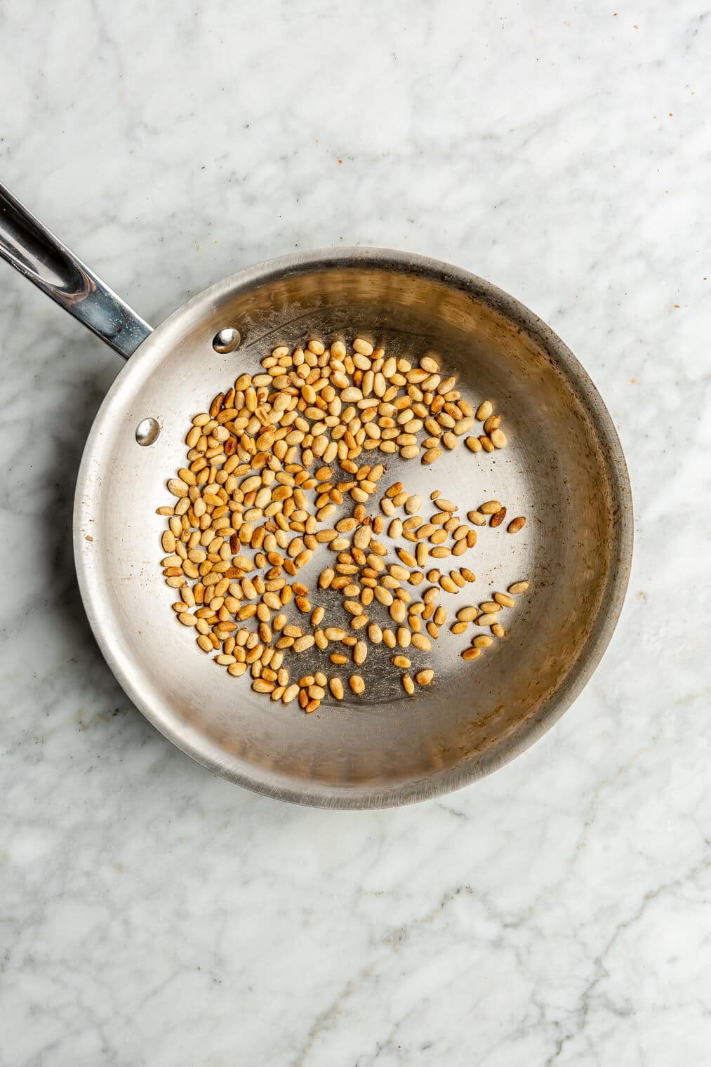 Pine nuts toasted in a small stainless steel pan.