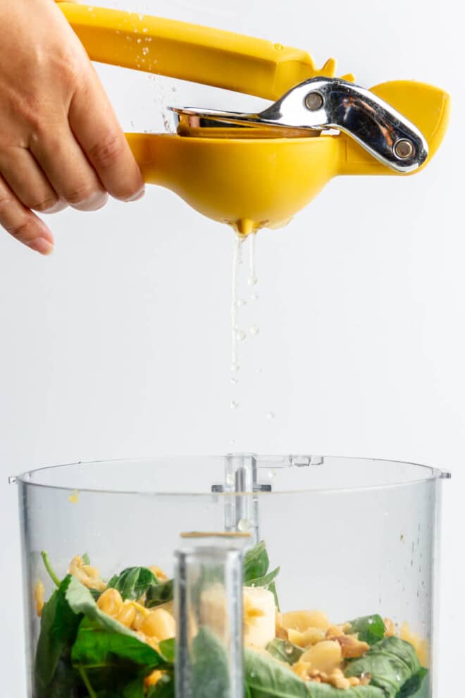 A lemon being juiced using a bright yellow citrus juicer into a food processor.