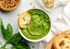 A small toasted piece of bread sitting in a bowl of roasted garlic pesto.