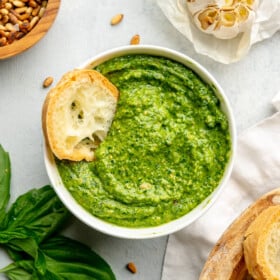 A small toasted piece of bread sitting in a bowl of roasted garlic pesto.