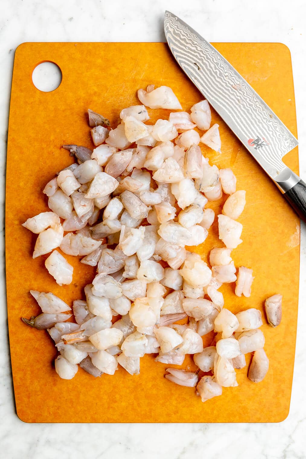 Chopped raw shrimp on a cutting board.